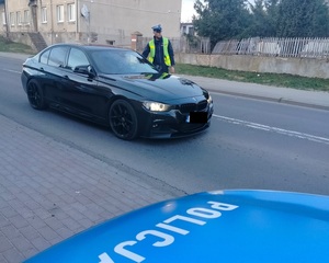 policjant stoi przy zatrzymanym pojeździe i sprawdza stan trzexwości kierowcy