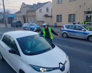 policjant stoi przy zatrzymanym pojeździe i sprawdza stan trzexwości kierowcy