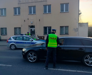 policjant stoi przy zatrzymanym pojeździe i sprawdza stan trzexwości kierowcy
