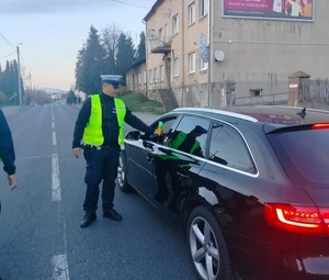policjant stoi przy zatrzymanym pojeździe i sprawdza stan trzexwości kierowcy