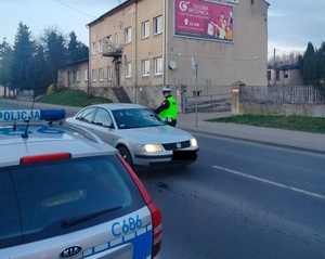 policjant stoi przy zatrzymanym pojeździe i sprawdza stan trzexwości kierowcy