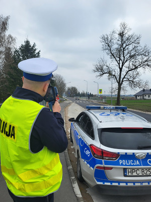 policjant stojący przy radiowozie i trzymający w reku miernik prędkości