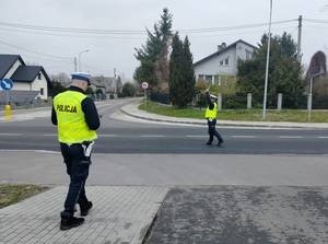 dwóch policjantów, jeden z nich stoi na jezdni i podnosi reke wydając polecenie do zatrzymania