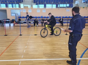 jeden z uczestników pokonuje tor przeszków, obok stoi policjant