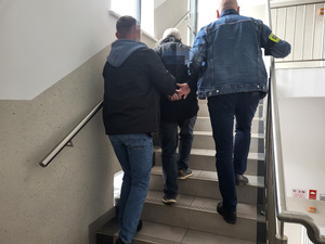 dwóch policjantów prowadzi zatrzymanego mężczyzne po schodach