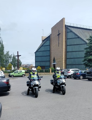 dwóch policjantów na motocyklach stojących na parkungu przed kosciołem