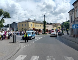 policjant stoi przy radiowozie na drodze,gdzie przechodzi procesja