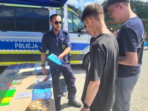 policjant prezentuje ulotke dwóm osobom stojącym przy policyjnym stanowisku