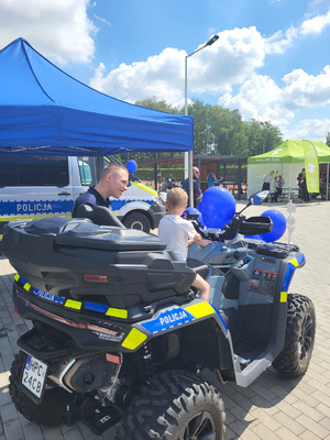 dziecko siedzące na quaDZIE, OBOK stoi policujant