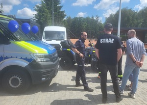 policjant przy policyjnym radiowozie rozmawia z uczestnikami