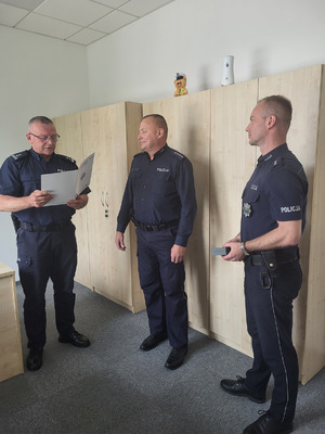 trzech policjantów, jeden z nich odczytuje list gratulacyjny