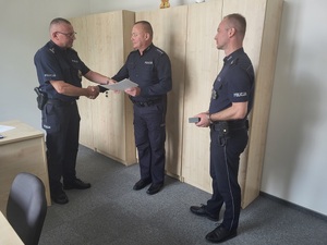 trzech policjantów, jeden z nich podaję reke i wręcza list gratulacyjny