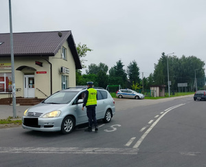 policjant stoi policjant stoi przy pojeździe i bada stan trzexwości kierowcy
