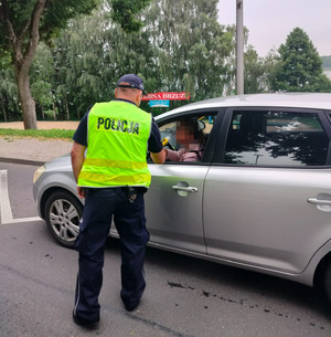 policjant stoi policjant stoi przy pojeździe i bada stan trzexwości kierowcy