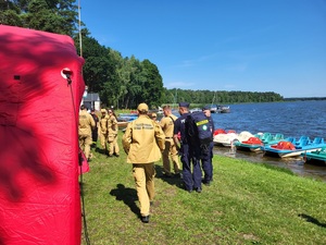 policjanci i strażacy stoja na plaży przy jeziorze