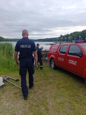 policjant oraz strażak na brzegu jeziora przygotowuja łódź do wodowania