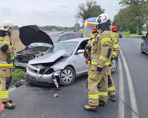 dwa pojazdy z uszkodzeniami, oraz stojący przy nich strażacy