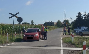policjant i pracownik kolei stoja przy pojeździe,który zatrzymała się przed przejazdem kolejowym