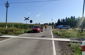 policjant i pracownik kolei stoja przy pojeździe,który zatrzymała się przed przejazdem kolejowym