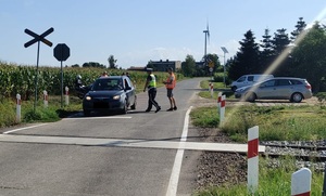 policjant i pracownik kolei stoja przy pojeździe,który zatrzymała się przed przejazdem kolejowym