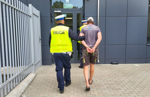 dwóch policjantów prowadzi mężczyzne w kajdanach