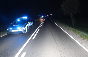zdjecie miejsca wypadku drogowego, gdzie widać na drodze stojący radiowóz,policjantów i ciągnik rolniczy