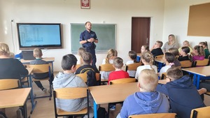 policjant stoi przed uczniami w klasie i prowadzi prelekcje