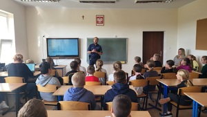 policjant stoi przed uczniami w klasie i prowadzi prelekcje