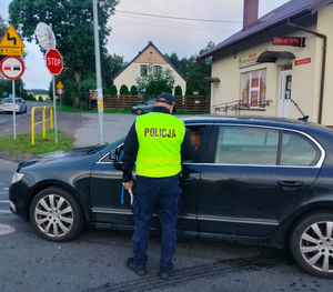 policjant stoi przy pojeździe i bada stan trzexwości kierowcy