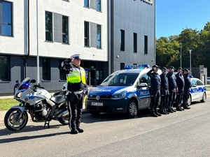 szeciu policjantów stojących na tle budynku przy radiowozach i oddaja honor