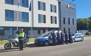 szeciu policjantów stojących na tle budynku przy radiowozach i oddaja honor