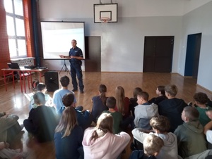policjant stoi na sali gimnastycznej przez uczniami i prowadzi prelekcję