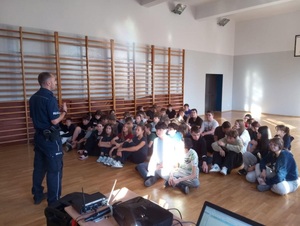 policjant stoi na sali gimnastycznej przez uczniami i prowadzi prelekcję