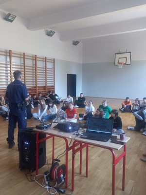 policjant stoi na sali gimnastycznej przez uczniami i prowadzi prelekcję